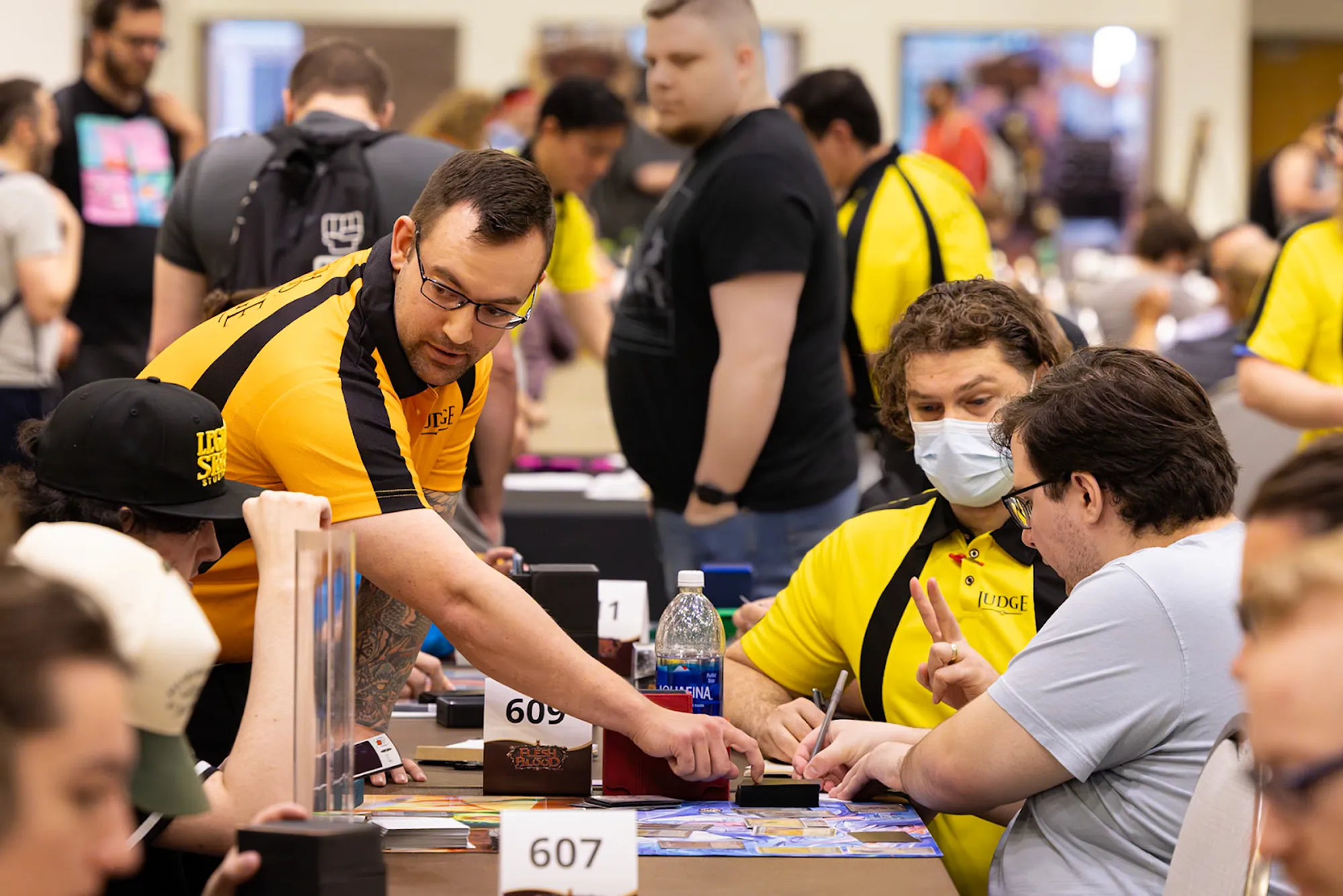 Two FaB judges, one in the yellow polo and the other in the orange Head Judge polo, answering a question for a player.